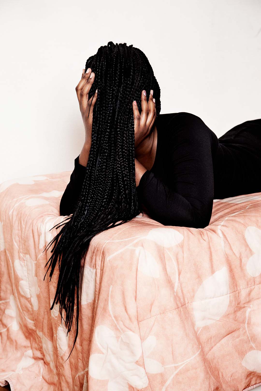 Photo of a woman laying on her front on a bed with her braided hair covering her face