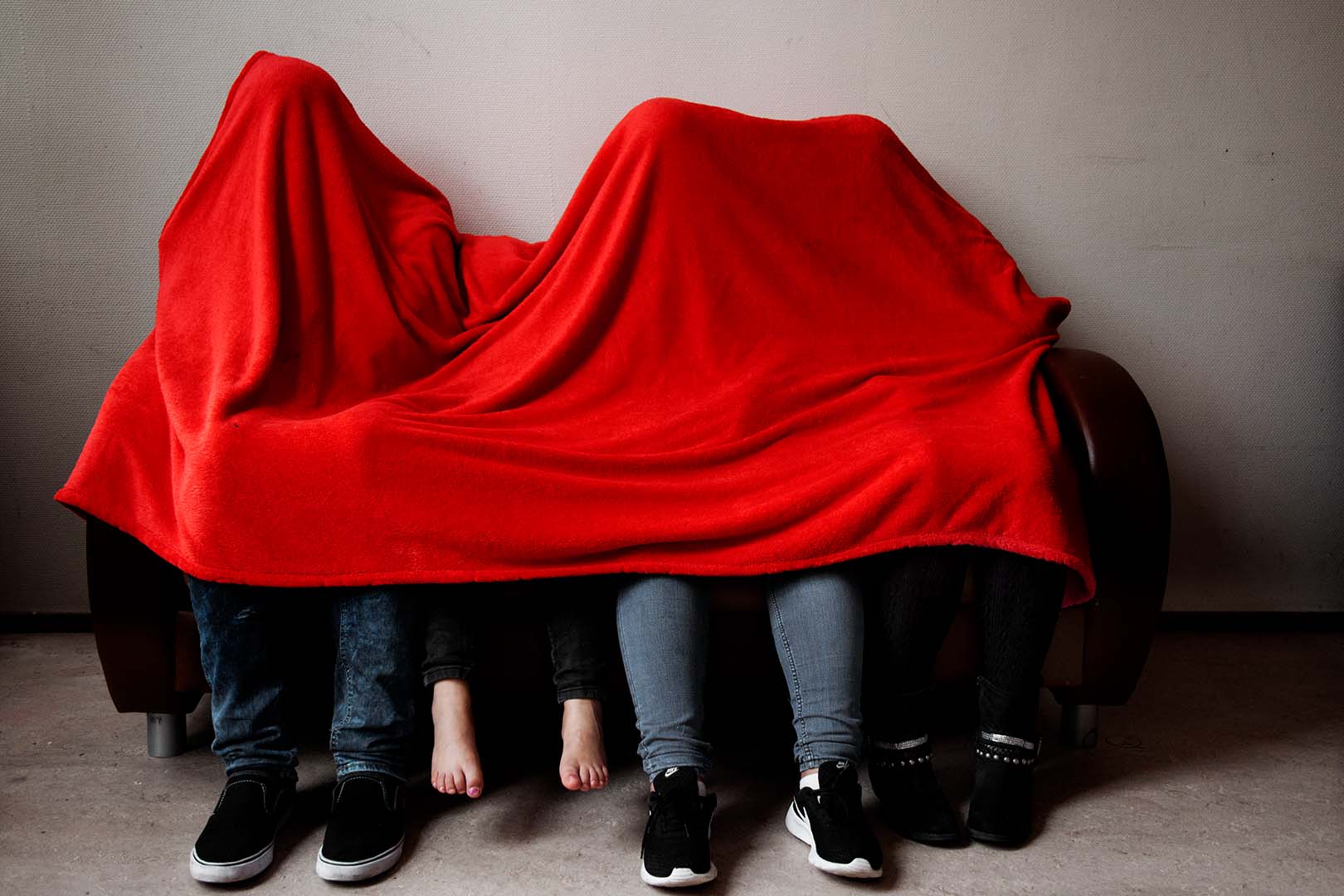 A family of four sits under a red blanket