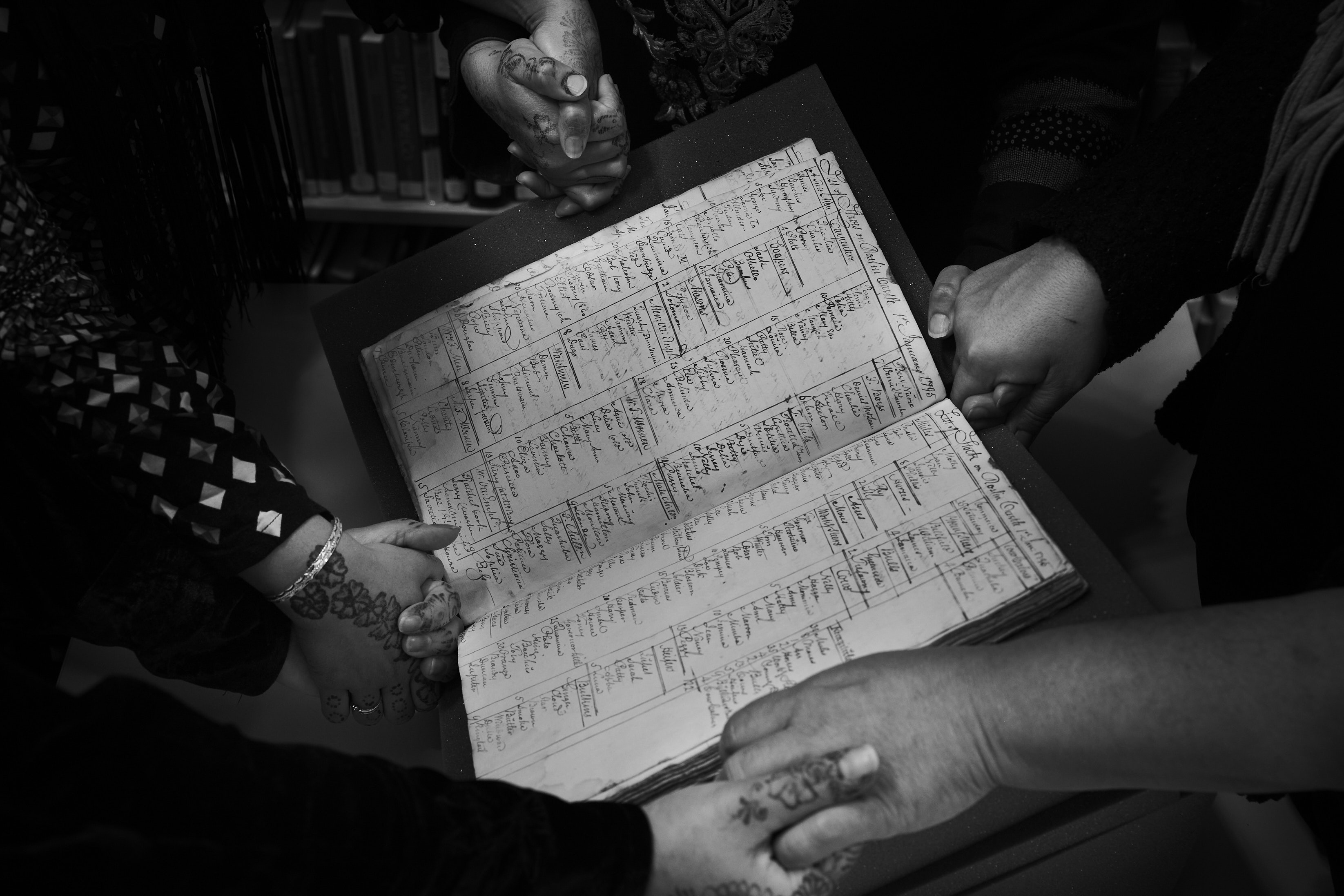 Black and white photo of people holding hands around an old slavery ledger
