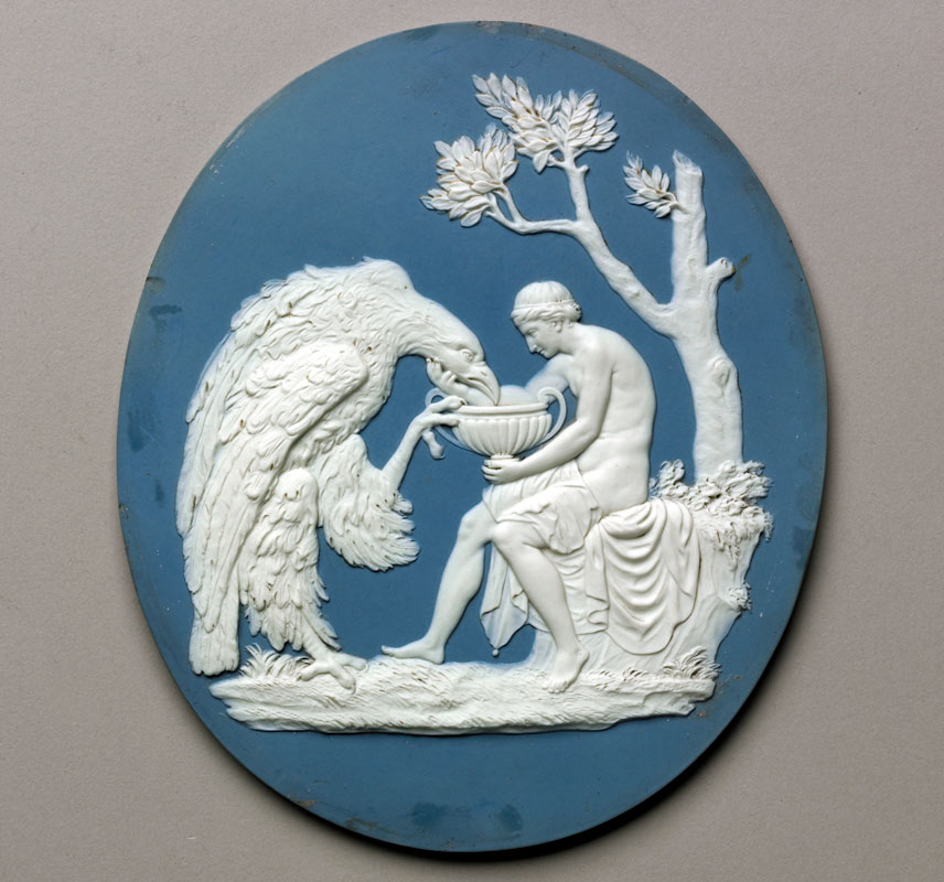 man gently cradling the chin of a huge eagle, leaning towards a large cup in his other hand, in a relief sculpture on a blue Wedgwood plaque