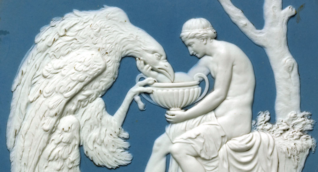 man gently cradling the chin of a huge eagle, leaning towards a large cup in his other hand, in a relief sculpture on a blue Wedgwood plaque