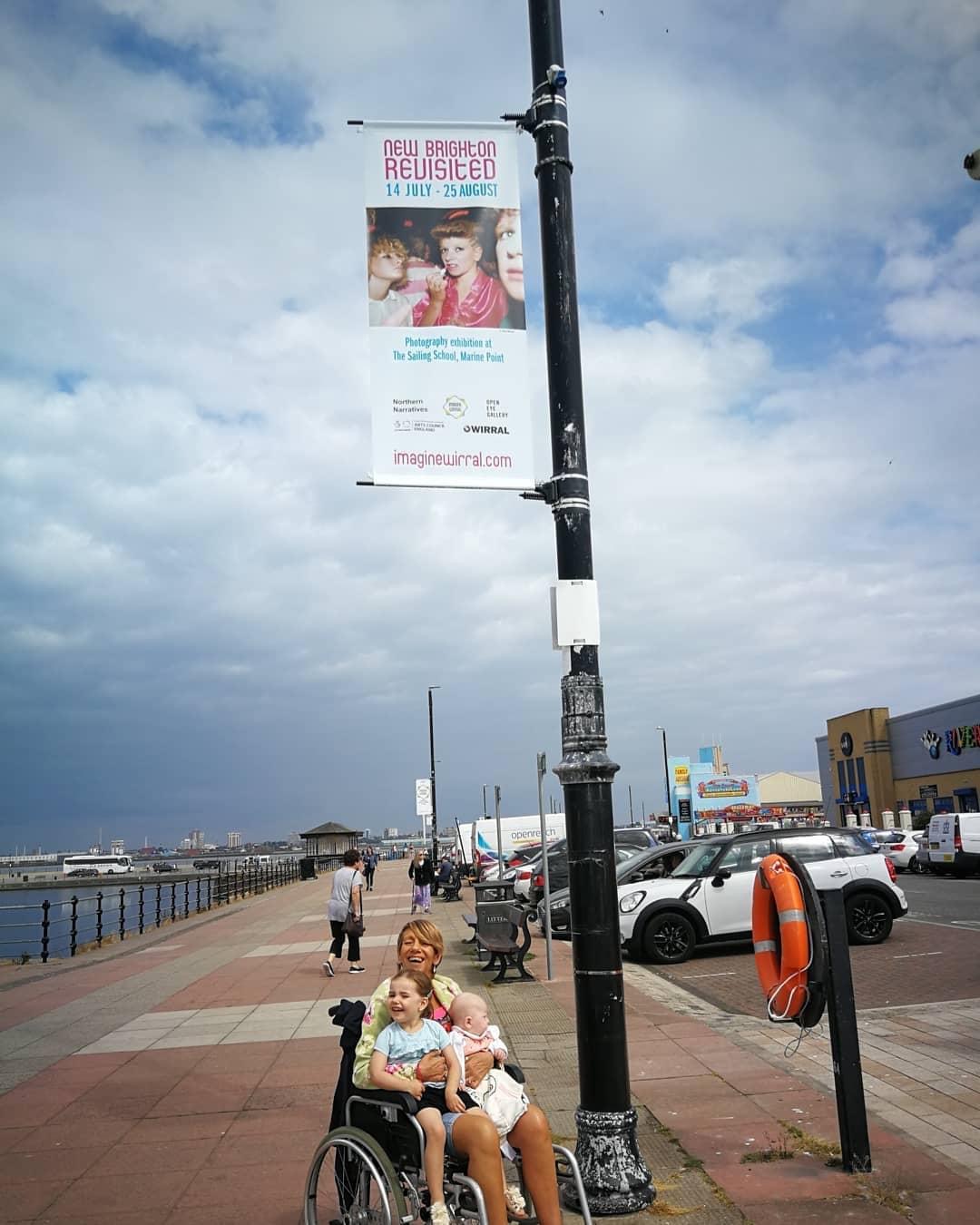 Photo of a woman in a wheel chair with a child on her lap below a banner with her photo on it