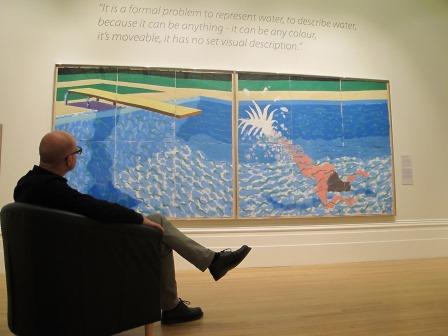 Image of man sitting in front of David Hockney painting