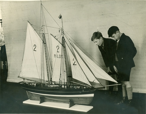 A model ship with sails being studied by two young boys in school uniform