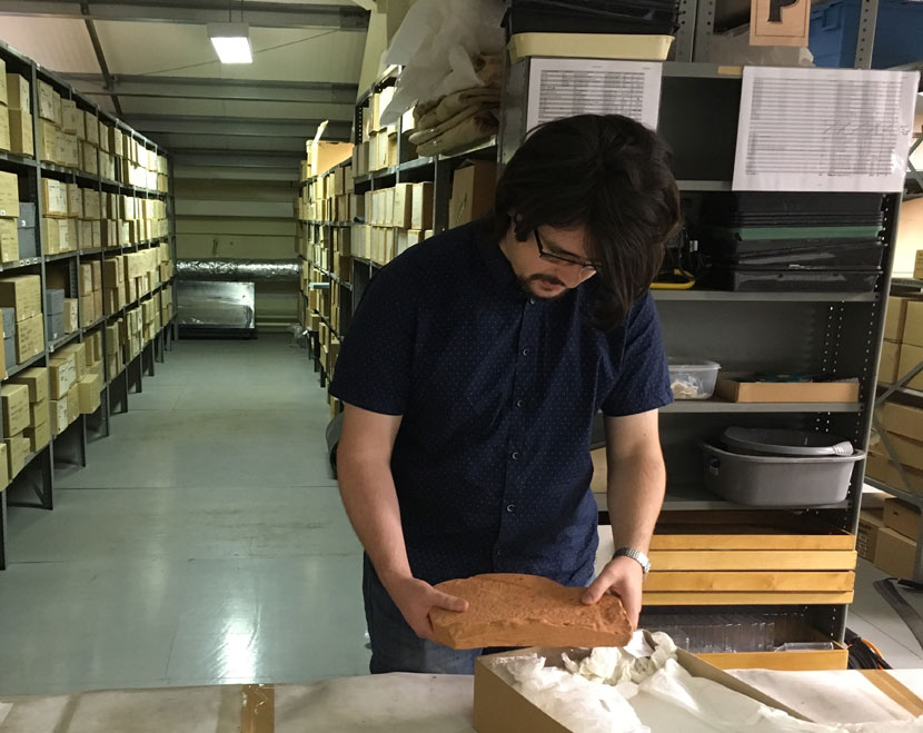 man examining archaeological finds in a large room full of boxes on shelves
