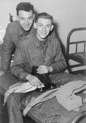 two men in army uniform, sat together on a bed