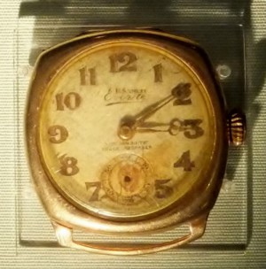 Gold coloured wrist watch missing its strap. Hands stopped at ten past three.