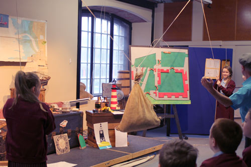 children using ropes to lift a large sack in a museum demonstration