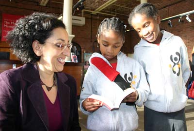 a woman crouching down to talk to two little girls reading a book