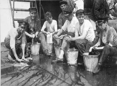 Black and white photo of men washing fabric in buckets on deck of a ship