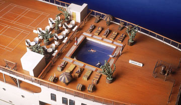 detail of the deck of a model ship showing passengers on deckchairs and swimming in the pool