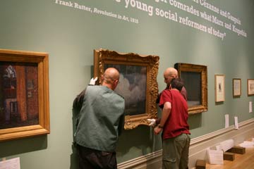 Three men hang a painting on a gallery wall