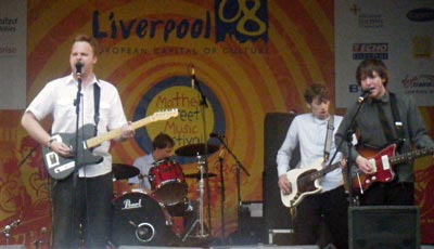A group of four men playing guitars and drums on a stage