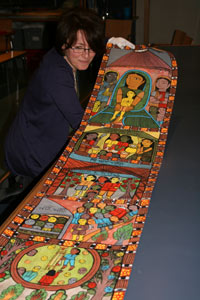 Lady with glasses looks at a long scroll with bright painted pictures on