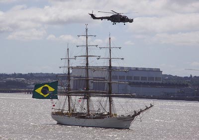 photo of a masted ship on a river with a helicopter flying above it