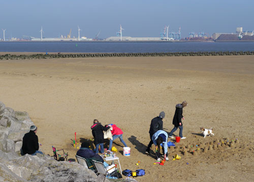 recent photo of people on a beach in winter clothing making sand castles