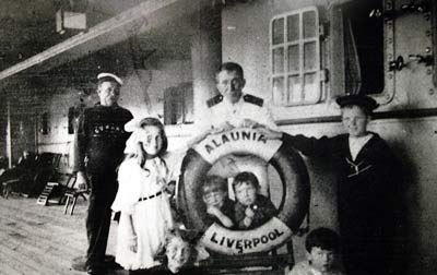 Black and white photo of children and members of crew posing on deck with a life ring rading 'Alaunia, Liverpool'