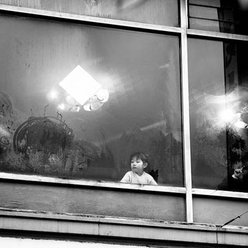 Black and white photograph of young girl looking out from an upstairs window