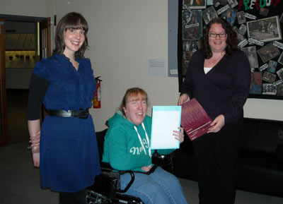 three smiling women, one holding up a certificate
