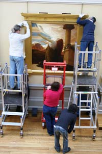 People on scaffolding and ladders hang a large painting