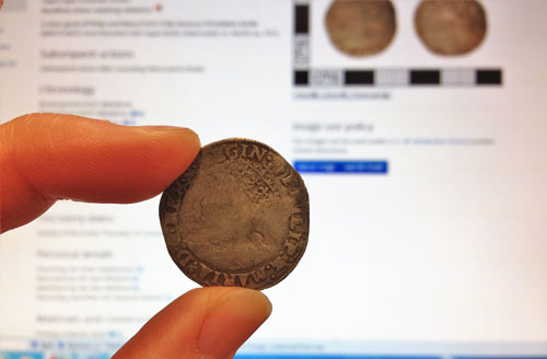 old coin held in front of screen showing coins in the database