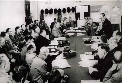 Black and white photo of men in uniform sitting around a board table.