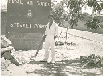 old photo of a man in cricket whites by the sign for an RAF base