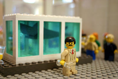 A suited lego man stands before a lego shark in a lego fishtank