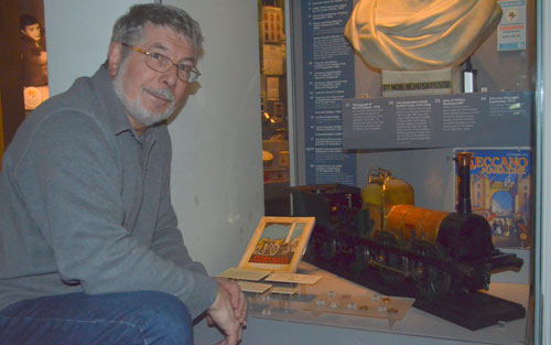man next to train model in museum display