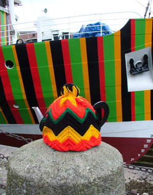 colourful tea cosy in front of a ship painted with a similar pattern