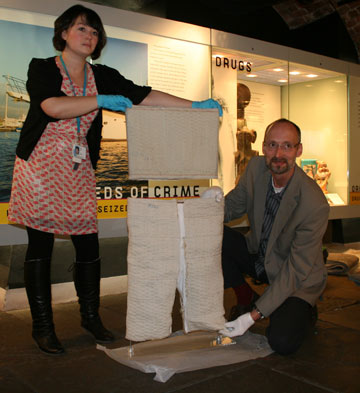 two curators holding up a body wrap and trousers with pockets for hiding drugs