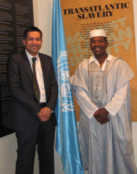 Two smiling men, one in a suit, the other in traditional African clothing, in front of display panels