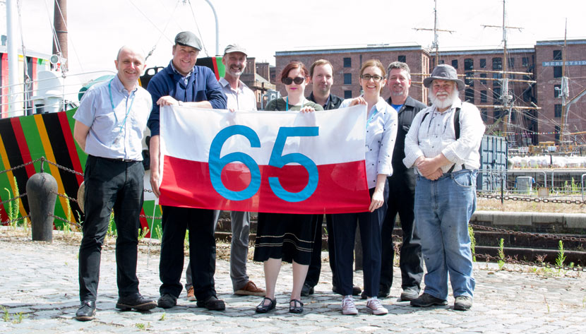 museum staff holding up a flag with 65 on it