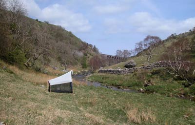 colour photo of a rural valley with a tent-like structure in the foreground and a viaduct in the background
