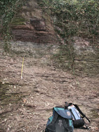 A layered rock face with ruck sacks in the foreground