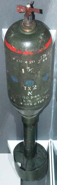 Photo of an old green bomb with fadded white lettering on the casing