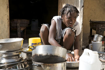 Young girl squatting to clean a large pile of pots and pans
