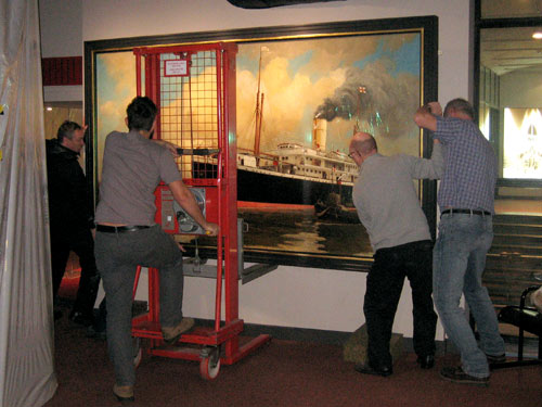 men with lifting equipment hanging a large painting on a wall