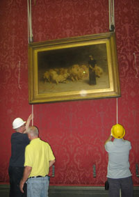 two men in hard heights lifting a painting with ropes and pulleys