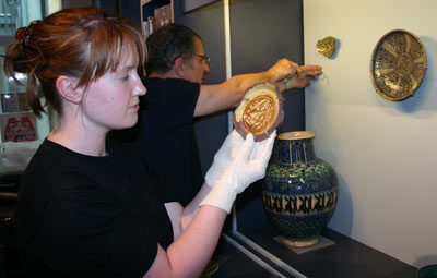 woman holdind up a piece of pottery while a man screws a wire support to a wall
