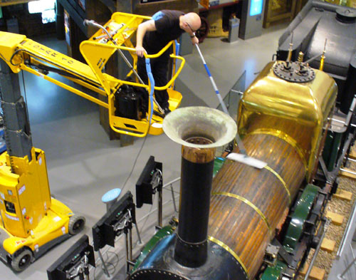 man in a small crane dusting an old train in the museum