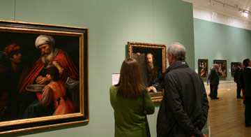 Two people look at a painting on a wall