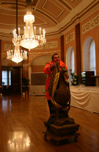 Man wheeling Liver Bird sculpture through a ballroom