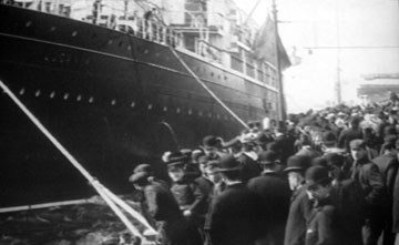 Black and white photo of crowds on a dockside beside a liner. 