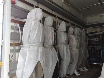 row of covered mannequins strapped inside a van in a standing position, with their shoes showing from under the sheet