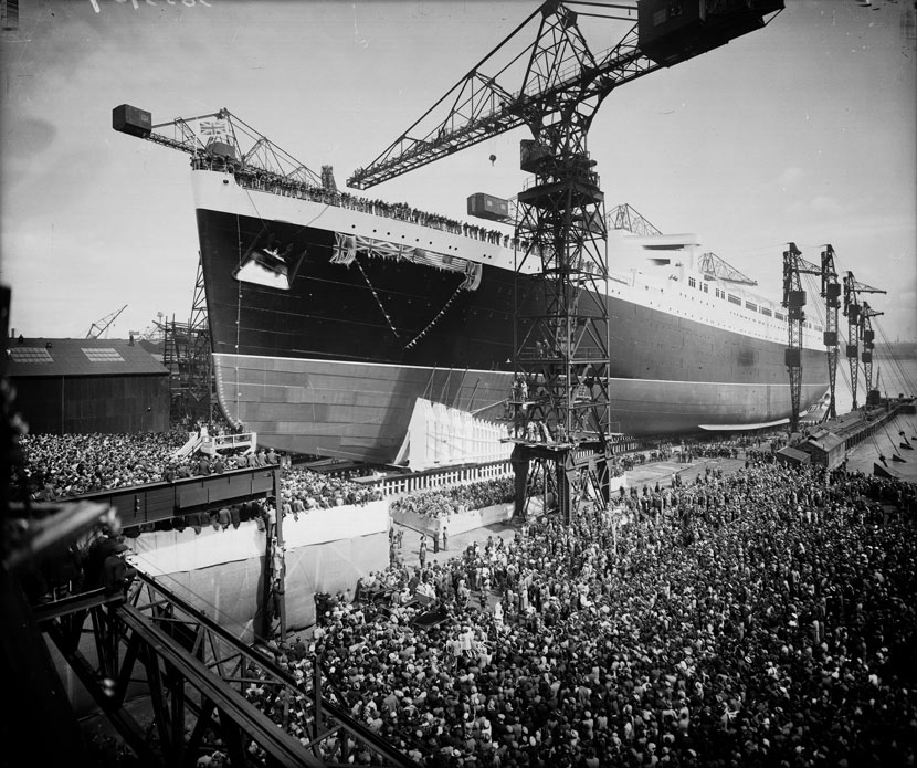 huge ship supported by cranes with thousands of people watching