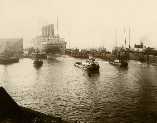Large ship being led into docks by 3 small tugs