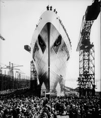 Black and white photo of the bow of a ship on a runway. There are crowds around.