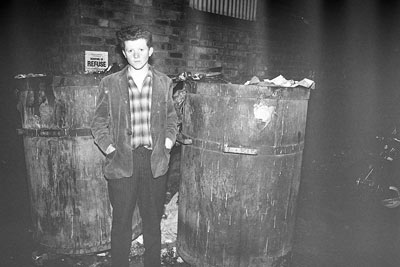 young man by large bins in a back alley
