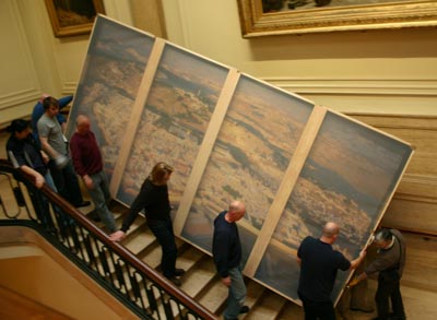 People carrying a large painting down a grand staircase